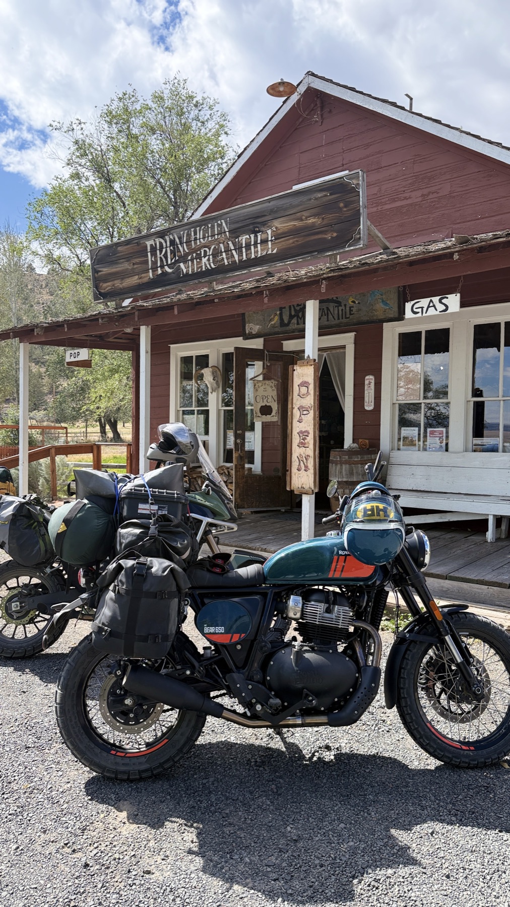 A teal Royal Enfield Bear 650 loaded with camping gear, parked in front of the Frenchglen Mercantile