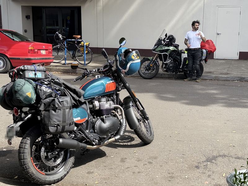 Royal Enfield Bear 650 loaded with camping gear on a city street, with a rider and a green Honda behind it
