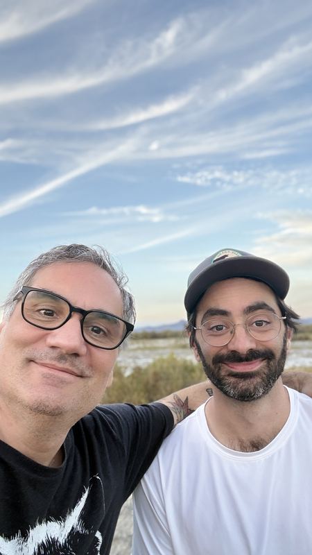 Two riders in a selfie with wispy clouds behind them