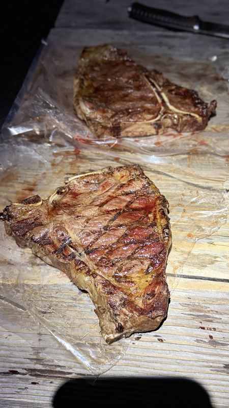 Two grilled T-bone steaks on a wooden table at night