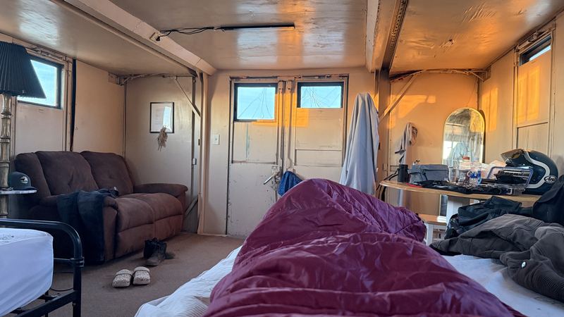 Inside a rustic cabin with a sleeping bag on the bed and gear on the table