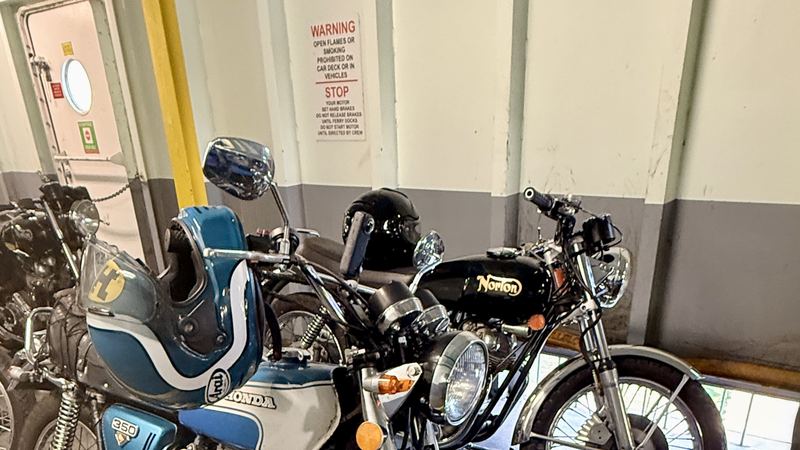 A blue Honda 350 and a Norton parked on a ferry car deck
