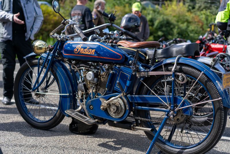A blue vintage Indian motorcycle with spoked wheels among a crowd of parked bikes