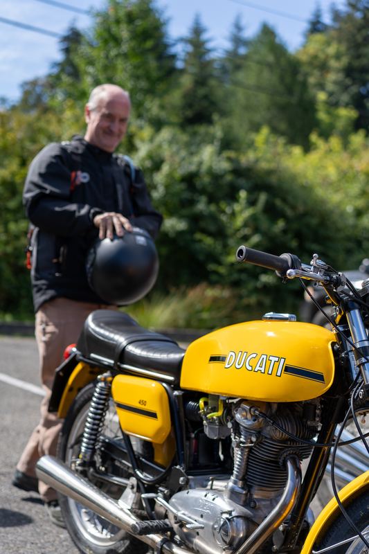 A rider holding a helmet beside a yellow Ducati