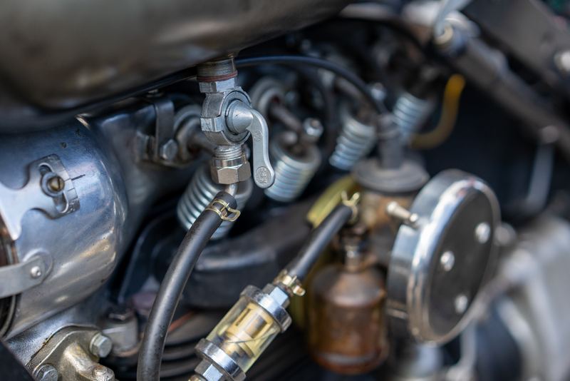 Close-up of a vintage carburetor and fuel fittings on a motorcycle engine