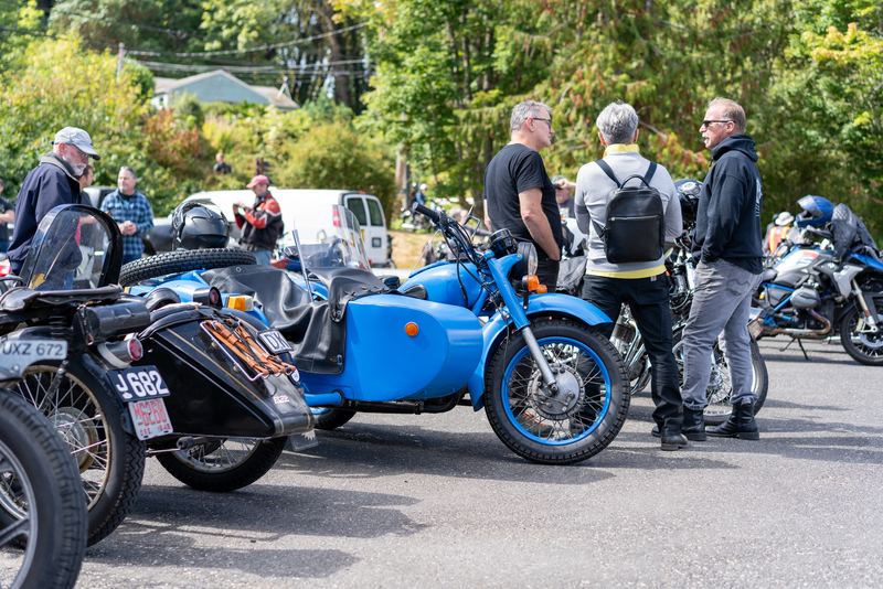 A blue sidecar motorcycle parked near a group of riders talking