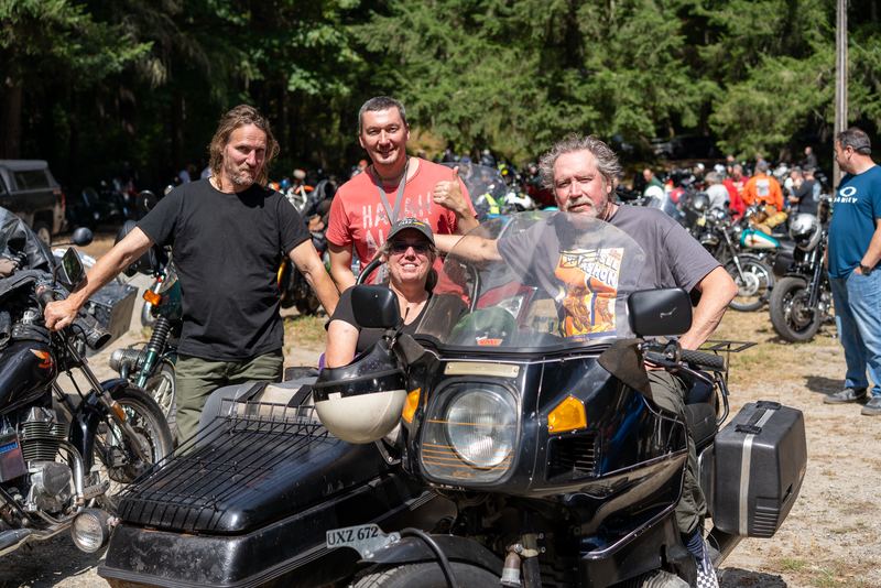 Three riders posing behind the windshield of a sidecar rig